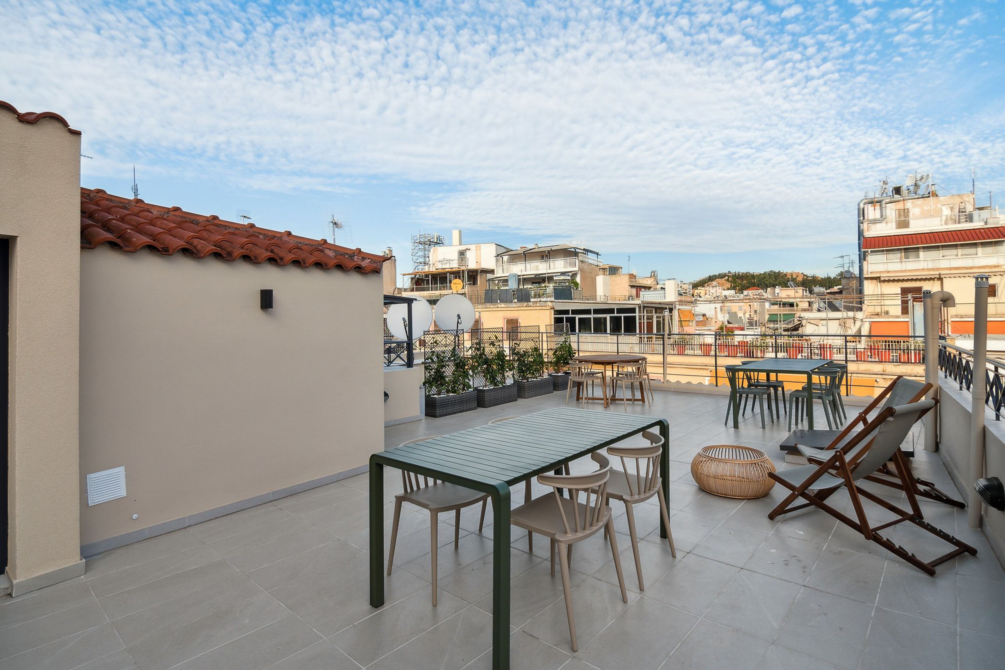 A rooftop terrace with a table and chairs, potted plants, and a view of surrounding buildings.