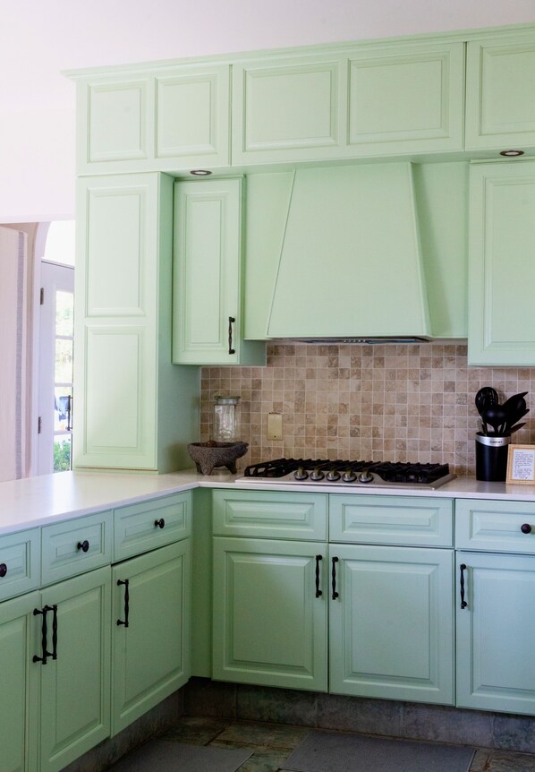 A kitchen with light green cabinets, a tiled backsplash, and a gas stove. - Designer Waterfront Villa with Sublime Views - Private & Exclusive. Free Kayaks. (Providenciales)