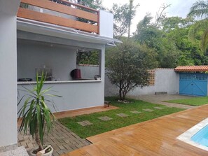 A modern outdoor kitchen area with a built-in grill, a small seating area, and a poolside setting.