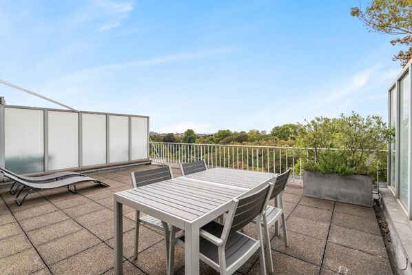 A rooftop terrace with a table and chairs, a sun lounger, and a view of greenery and buildings. - Fuths Loft Penthouse 85 (Antwerpen,)