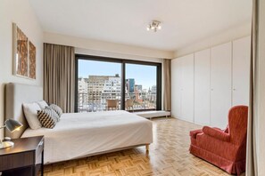 A modern hotel room with a large bed, a red armchair, and a city view through floor-to-ceiling windows. - Fuths Loft Penthouse 85 (Antwerpen,)