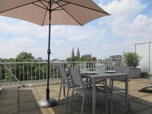 A rooftop terrace with a table set for dining, a large umbrella, and a view of a city skyline. - Fuths Loft Penthouse 85 (Antwerpen,)