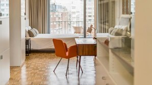 Habitació d'hotel moderna amb una finestra gran, un llit, una taula de fusta i cadires taronja.