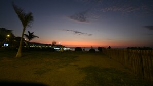 A nighttime view of a beach with a wooden fence, palm trees, and distant city lights. - Beautiful beachfront apartment a few minutes from the best Limeña beaches (Ciudad de Guatemala)