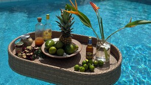 Cenário à beira da piscina, com uma bandeja flutuante de bebidas e frutas tropicais.