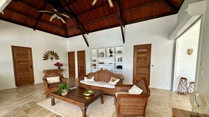 Uma sala de estar ampla, com teto alto, móveis de madeira e piso de azulejos.