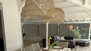 Uma sala de jantar com uma mesa comprida para seis pessoas, cadeiras brancas e um candeeiro de teto em tecido.