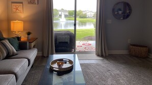 En stue med sofa, sofabord med skål, lampe og udsigt til et søo gennem en glasdør.