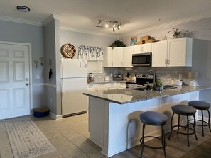 A modern kitchen with white cabinetry, a granite countertop, a built-in microwave, and a central island with bar stools. - Lovely/Serene/Water View1st floor 2B/2BA Condo,10M-Beach. (Conway)