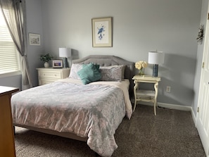 Une chambre à coucher avec un lit, deux tables de chevet, une lampe, un tableau encadré et une petite plante.