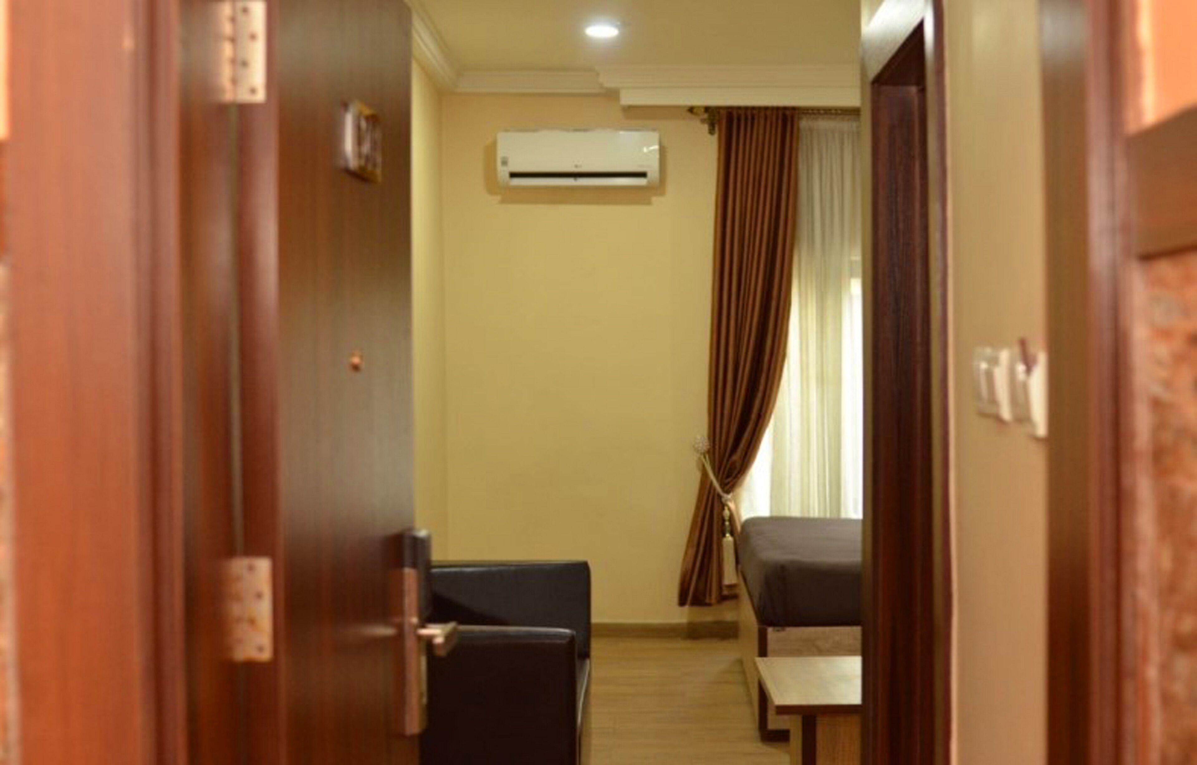 A hotel room with a bed, a small table, a chair, an air conditioning unit, and a curtain.