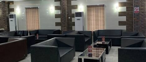 A modern lounge area with sofas and a coffee table, air conditioning units, and a no-smoking sign on the wall.