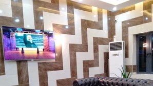 A lobby with a modern design, featuring a large flat-screen TV mounted on the wall, a black leather sofa, and a glass coffee table. - CASONI INTERNATIONAL HOTELS AND SUITES (Port Harcourt)