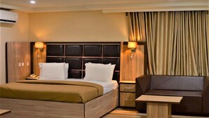 A hotel room with a large bed, a sofa, a nightstand, and a lamp. - CASONI INTERNATIONAL HOTELS AND SUITES (Port Harcourt)