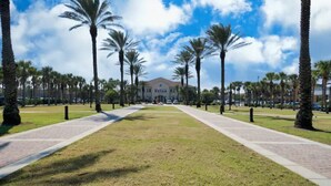 A pathway lined with palm trees leading to a building with a red roof. - Ocean Seaside Escape B
 (Jacksonville Beach)