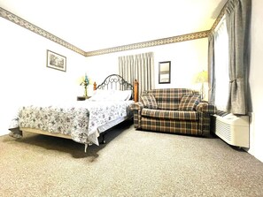 A bedroom with a bed, a sofa, a bedside table, a lamp, and a radiator. - Apt. 2 - Ensuite Bath, Roku, Fridge/Micro, Queen (Paulding)