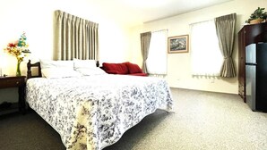 Hotellihuone, jossa on sänky, yöpöytä, lamppu, lipasto ja jääkaappi.