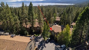 A residential area with houses surrounded by dense forest, a clear view of a lake and mountains in the background, and a red arrow pointing to a specific house. - Dollar Hill II # 25 by Hauserman Rental Group (Tahoe City)