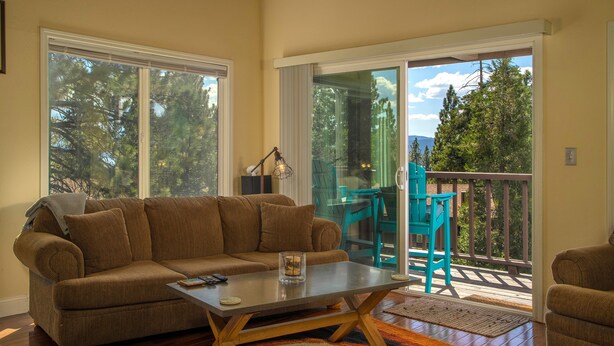 A living room with a brown sofa, a coffee table, and a view through a glass door to an outdoor deck. - Dollar Hill II # 25 by Hauserman Rental Group (Tahoe City)