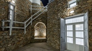 Un intérieur aux murs de pierre, avec un escalier, un banc et une porte.