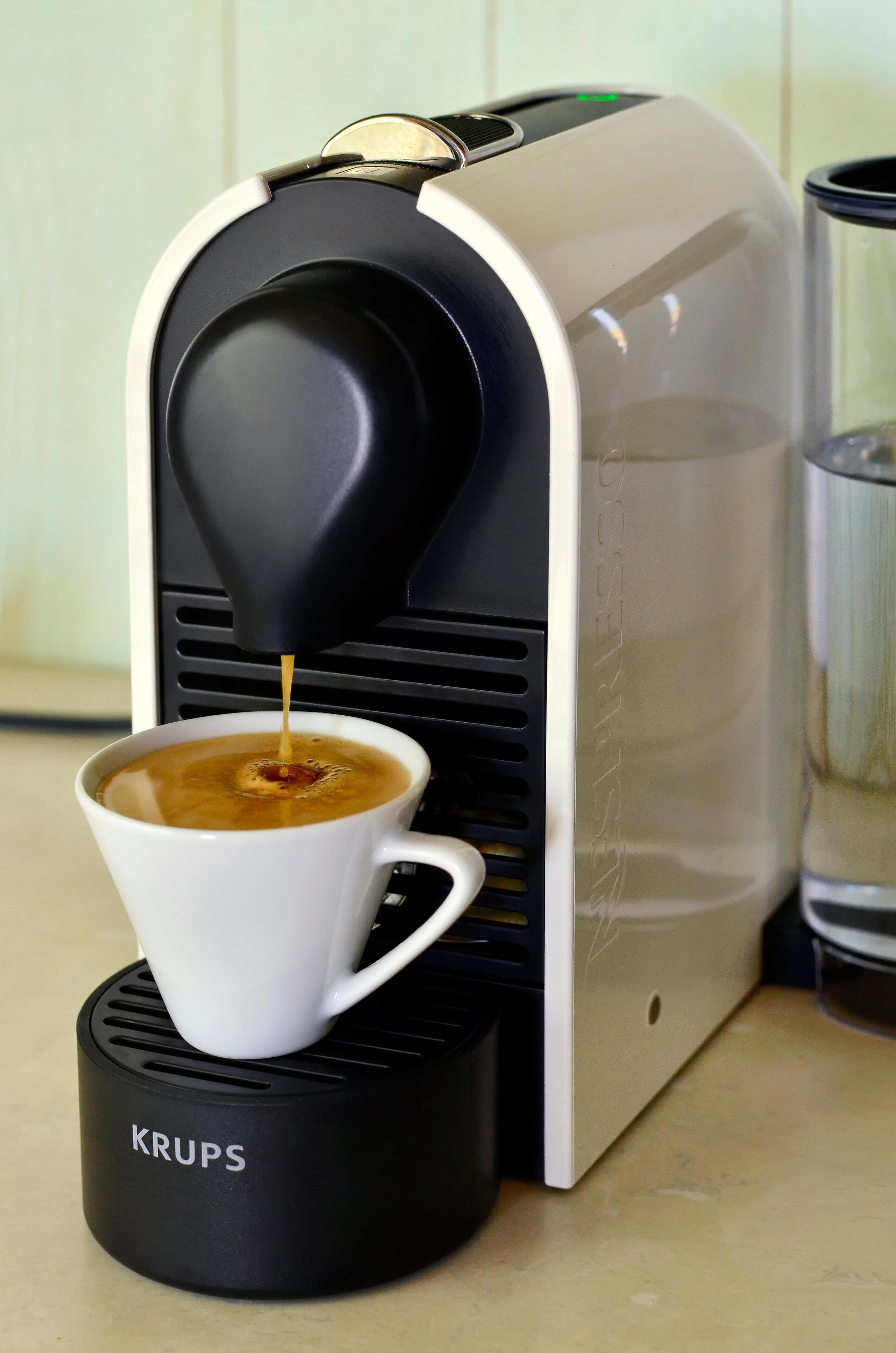 A Krups coffee machine dispensing coffee into a white cup.