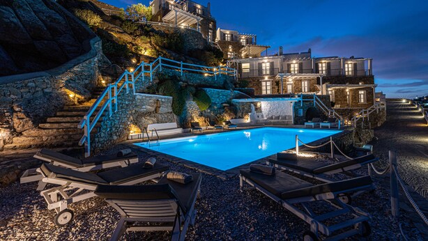 A pool area with lounge chairs, a stone staircase, and a building with multiple balconies. - Luxury VillaThelgoMykonos IV, amazing sea View! (Mykonos)