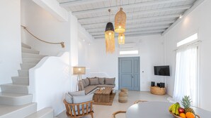 Una sala de estar moderna con una escalera, un conjunto de sofás, una mesa de comedor con fruta y un televisor.