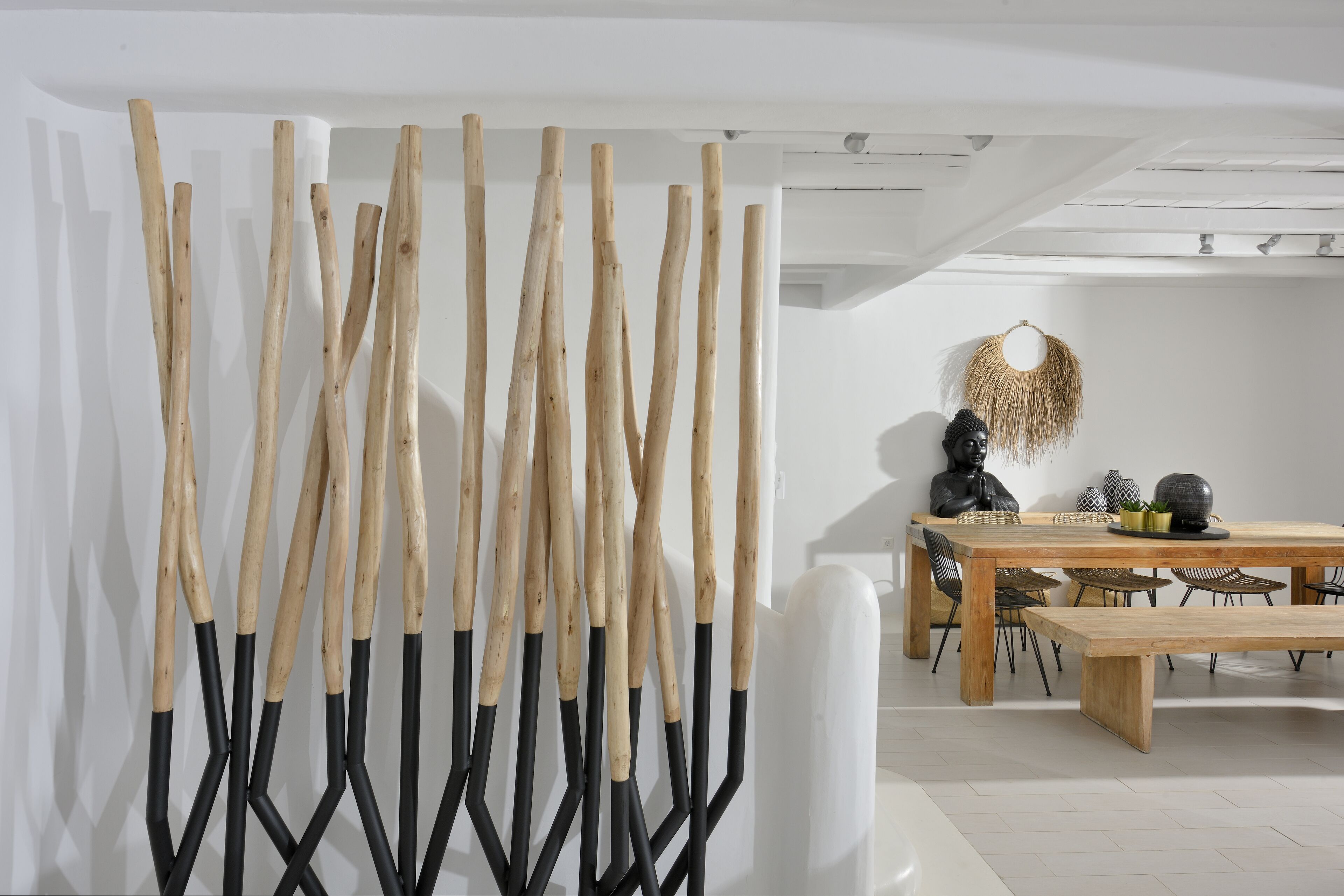 Una zona de menjador moderna amb una taula i caires de fusta, una paret blanca amb un penjoll decoratiu, i una banca blanca.