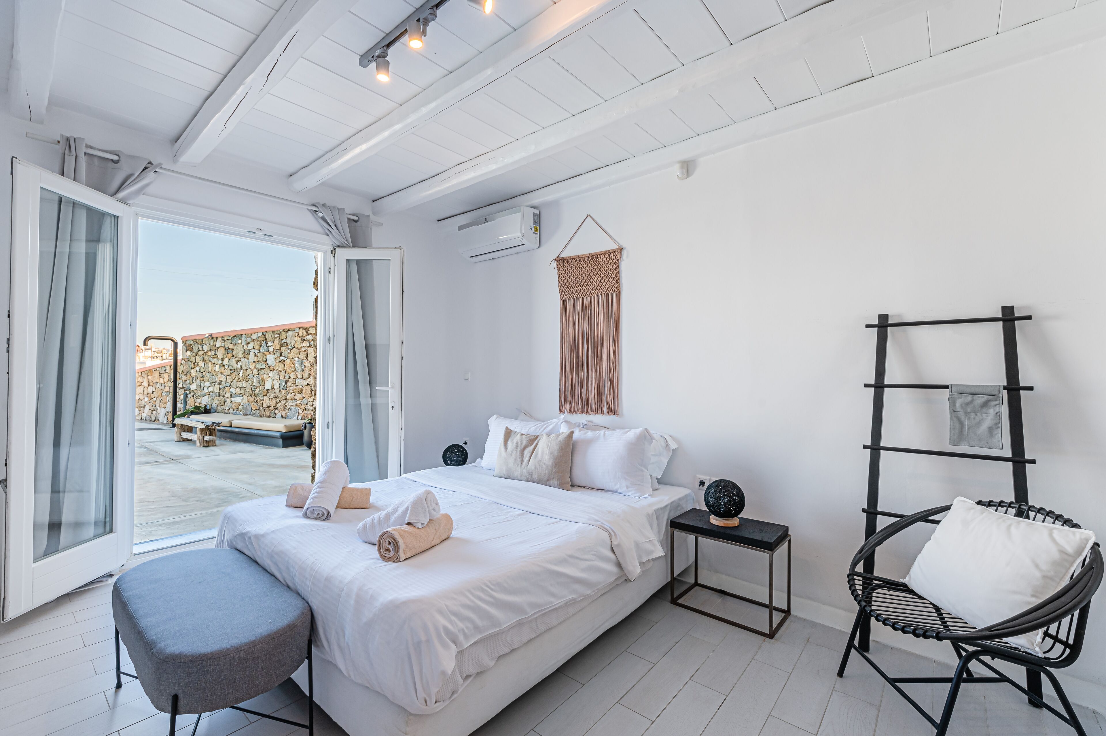 Ein Schlafzimmer mit einem Bett, einem Sessel, einem Nachttisch und Blick ins Freie.