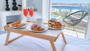 Un vassoio per la colazione con pasticcini, una tazza di caffè e due bicchieri di succo su un letto con vista sul mare.