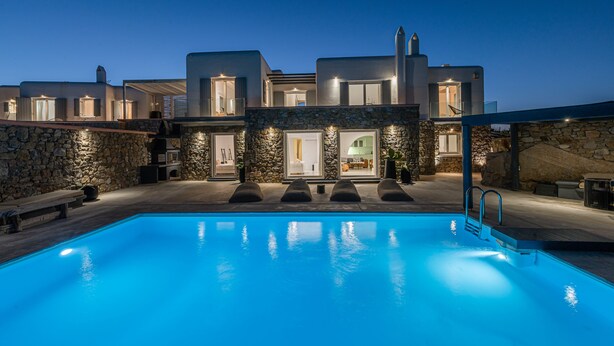 Una villa moderna con piscina, pareti in pietra e diversi ingressi.