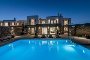 En modern villa med en swimmingpool, stenmurar och flera entréer.