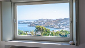 Ein Fenster mit Blick auf eine Küstenlandschaft, darunter ein Gewässer, Hügel und Gebäude.