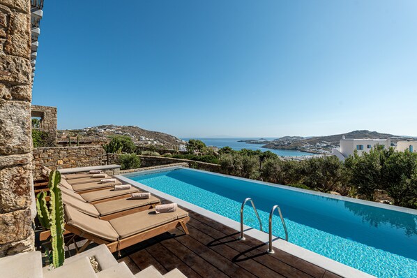 Piscina com espreguiçadeiras e vista para o mar.