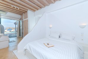 Een slaapkamer met een groot bed, een witte bank en uitzicht op een zwembad door een glazen deur.