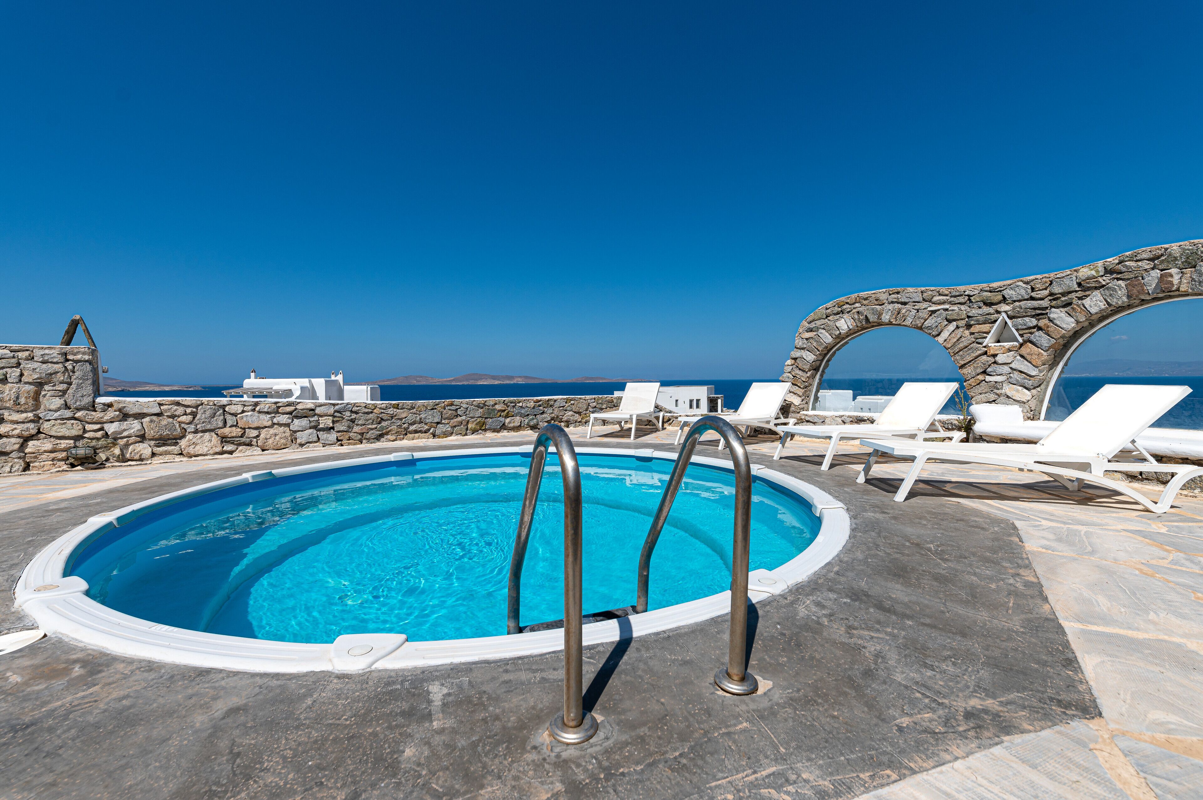 Une piscine avec des murs en pierre et des chaises longues blanches.