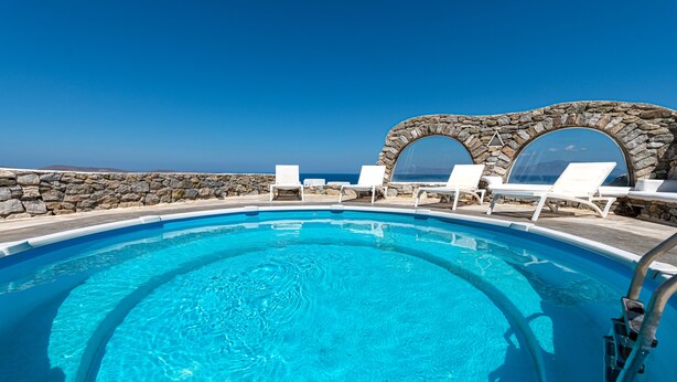 Une piscine d’un bleu éclatant, bordée de chaises longues blanches et agrémentée d’arches en pierre.