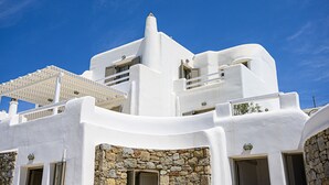 Un bâtiment blanc aux murs de pierre et aux balcons, sous un ciel bleu dégagé.