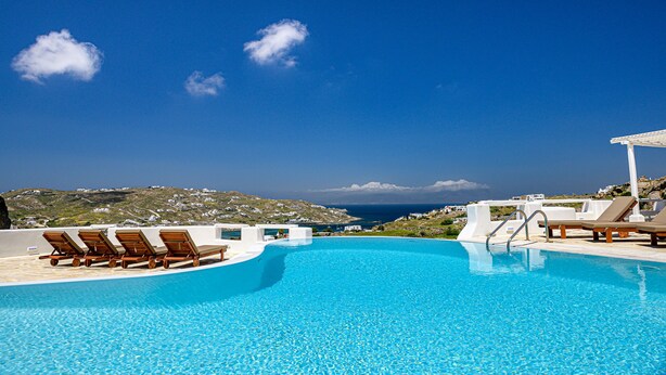 Un ciel d’un bleu éclatant, une piscine avec des chaises longues et une vue sur la mer et les collines.