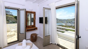 Une chambre d’hôtel avec un lit, une télévision, un miroir en bois et une vue sur un paysage côtier.