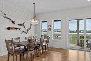 Ein Essbereich mit Holztisch und -stühlen, einer Chandelierleuchtre und Blick auf eine Terrasse und Wasser.