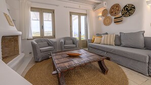 Un salon avec une cheminée, des canapés gris, une table basse en bois et une vue dégagée sur l’extérieur grâce à de grandes fenêtres.