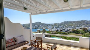 Une terrasse offrant une vue sur une ville côtière, une pergola blanche et un espace détente avec une table et des chaises.