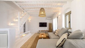 A modern living room with a staircase, a flat-screen TV, and a large grey sofa. - 9 Muses Villa Thalia 5 BR with private pool! (Mykonos)