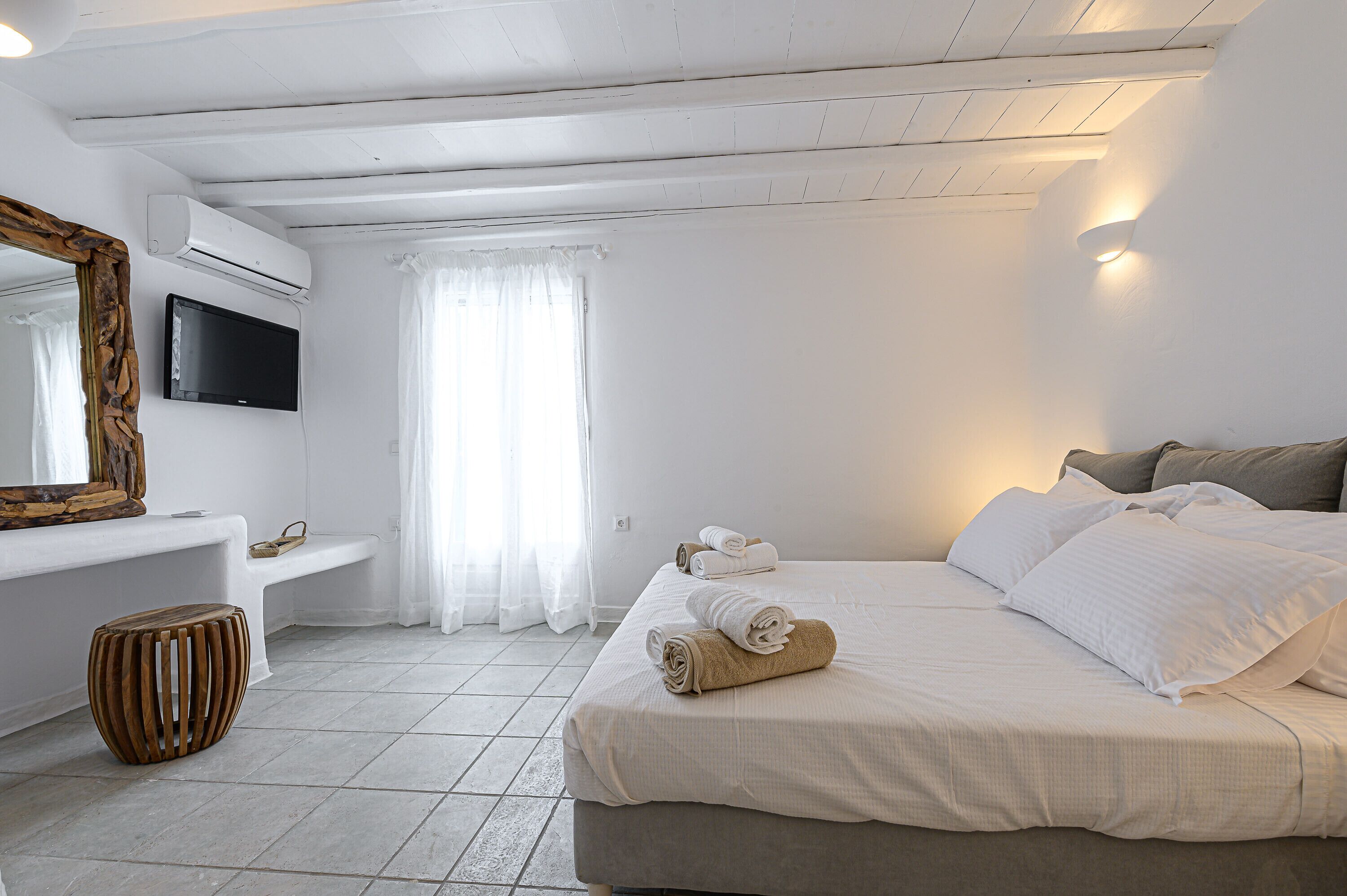 Een hotelkamer met een bed, een bankje, een televisie en een spiegel.