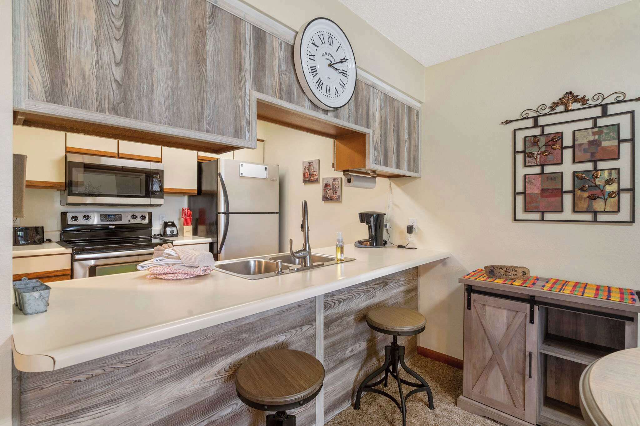 A kitchen with a wooden backsplash, a large clock, and a coffee machine.