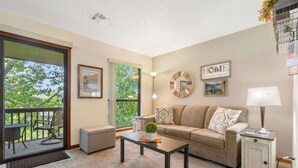 A living room with a sofa, coffee table, and a small side table. There is a sliding glass door leading to an outdoor area with a patio table and chairs. - The Cozy Place - Pointe Royale Condo Perfect for Couples! (Branson)