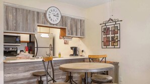 A kitchen with a wooden backsplash, a clock, and a dining area with four stools. - The Cozy Place - Pointe Royale Condo Perfect for Couples! (Branson)