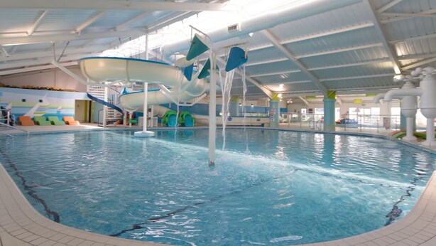 Una piscina interna con uno scivolo acquatico, sdraio e un affresco sulla parete.