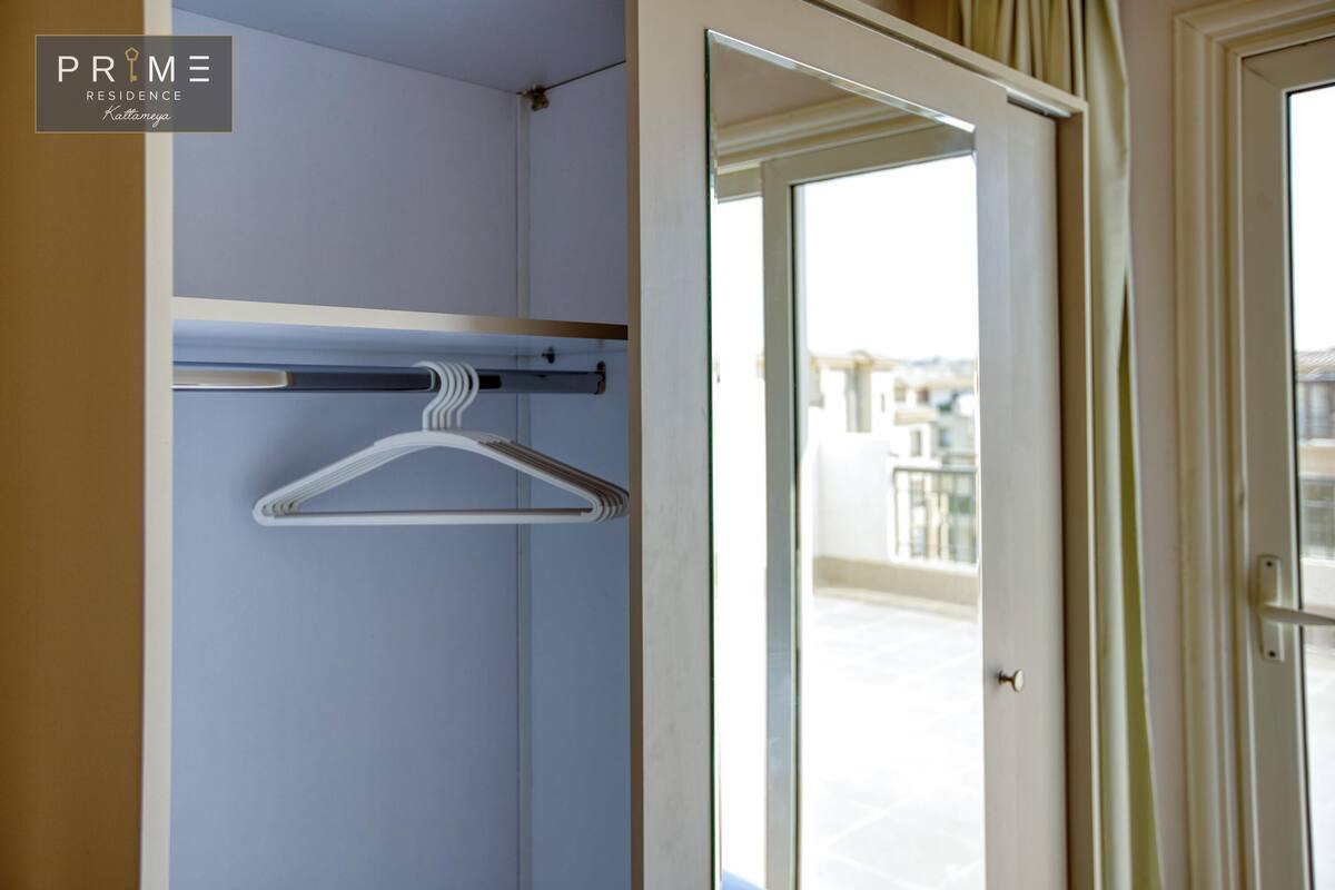 A hotel room with a hanging closet, a sliding glass door to the balcony, and a visible cityscape view.